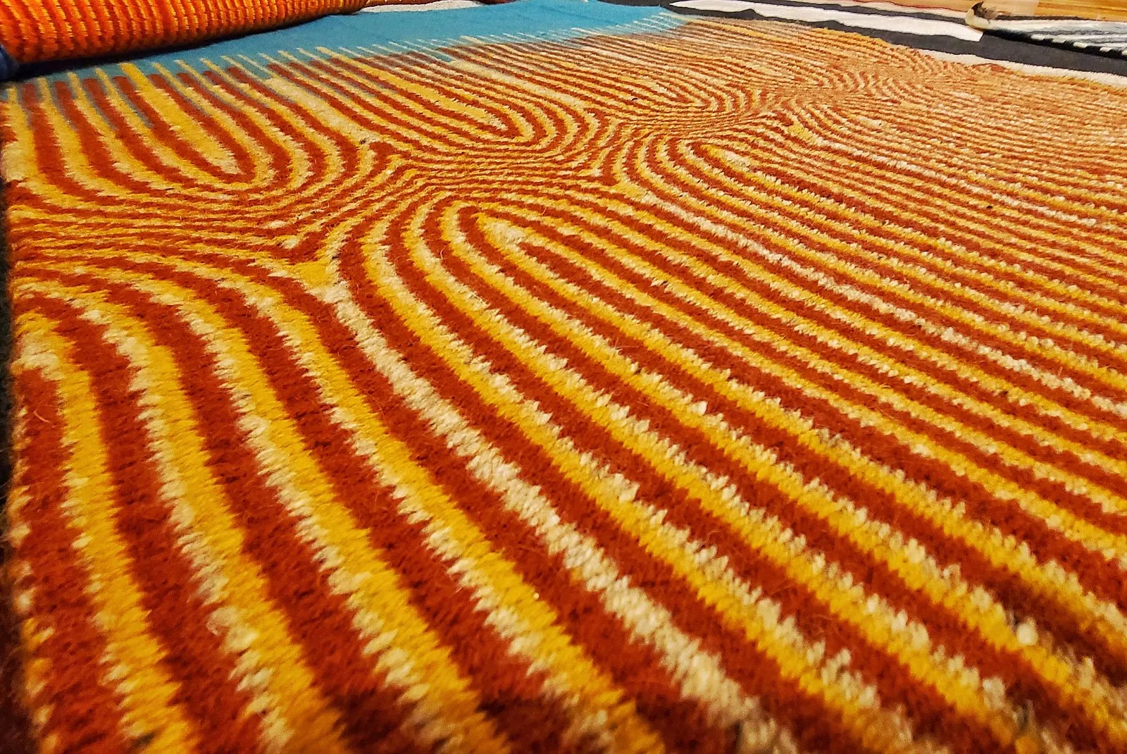 Close-up of a hand-woven rug by Charles H. Blanchard in curved bands of orange, gold and red with turquoise, showing the wool weave in detail