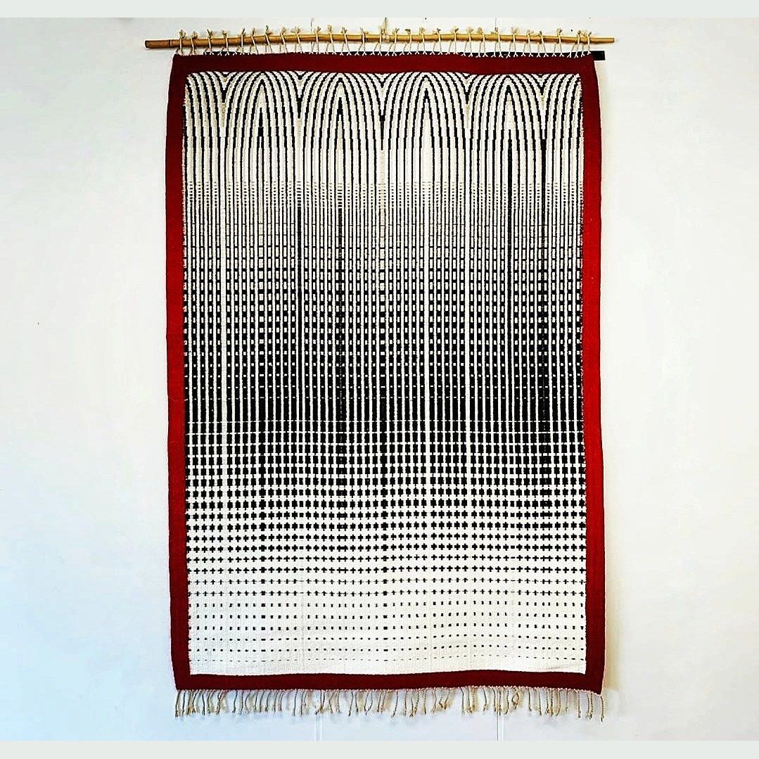 Hand-woven wall tapestry by Charles H. Blanchard, the Dyberry Weaver of Narrowsburg NY, with black arches dissolving into scattered dots on cream inside a deep red border, hung from a bamboo rod with cream fringe
