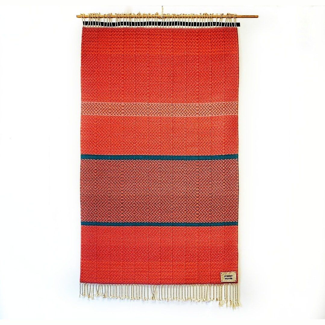 Hand-woven wall tapestry by Charles H. Blanchard, the Dyberry Weaver of Narrowsburg NY, in rust-orange herringbone weave banded by two teal stripes, hung from a bamboo rod with cream fringe and the Dyberry Weaver studio label