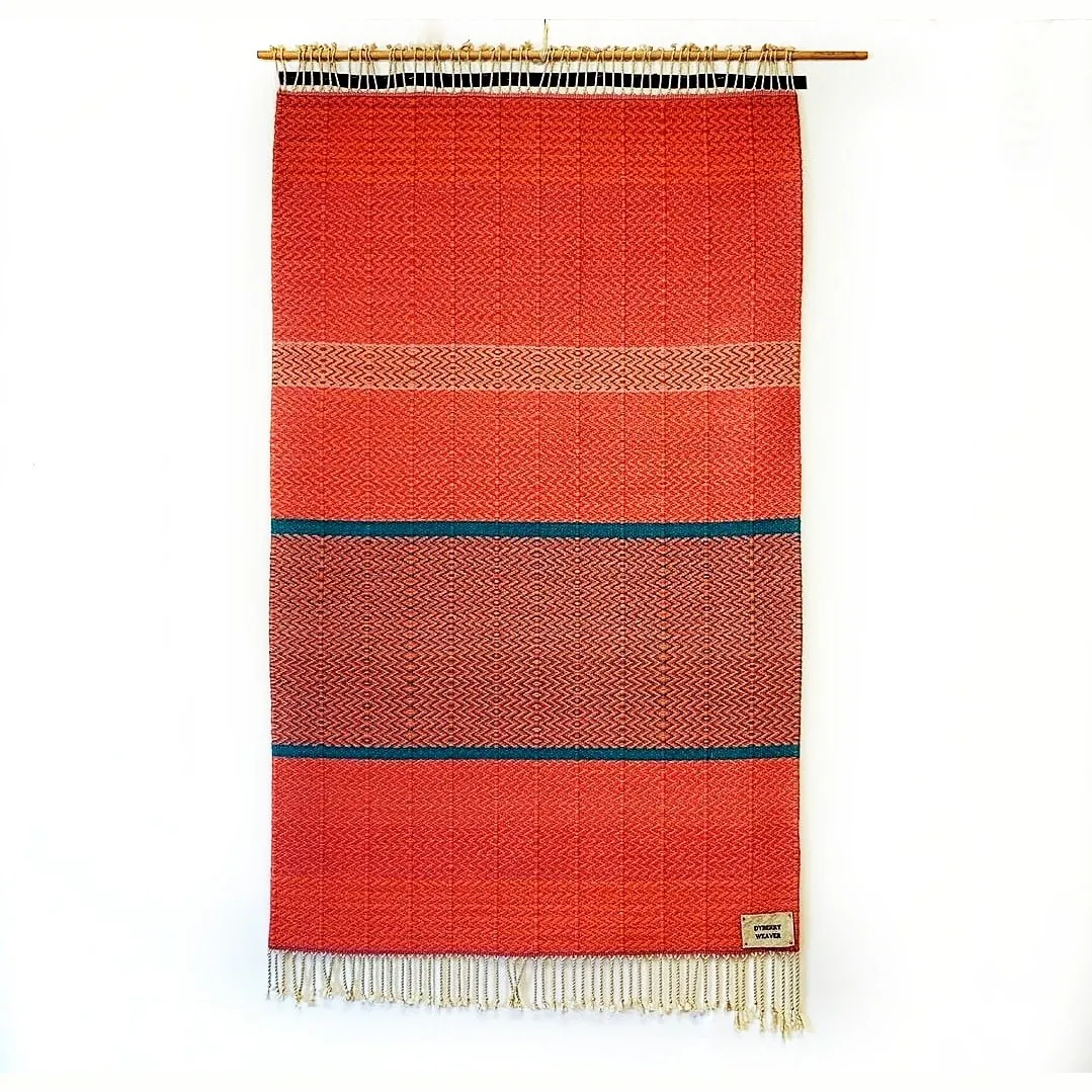 Hand-woven wall tapestry by Charles H. Blanchard, the Dyberry Weaver of Narrowsburg NY, in rust-orange herringbone weave banded by two teal stripes, hung from a bamboo rod with cream fringe and the Dyberry Weaver studio label