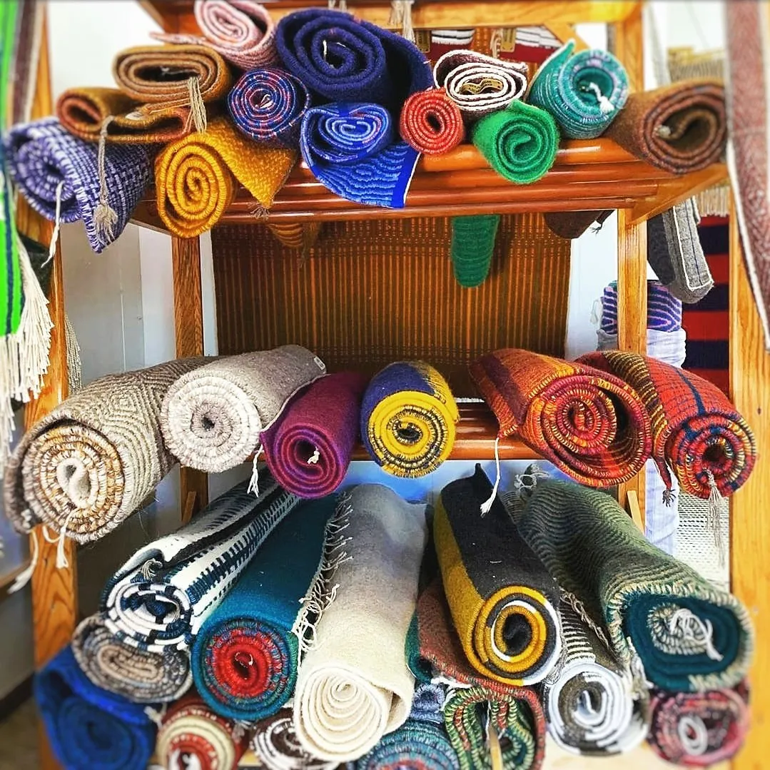 Rolled hand-woven rugs in many colors stacked on wooden shelves at the Dyberry Weaver studio in Narrowsburg NY